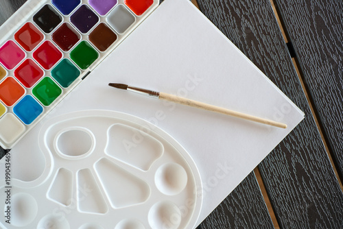 Colorful paint palette and brush placed on blank paper ready for creative work in an indoor setting during the daytime