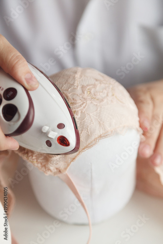 A close-up photo of a seamstress ironing a beige lace bra. Film grain added to the photo.