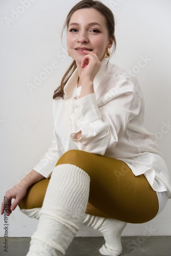 Young woman poses for a casual fashion look with white shirt and colored leggings in a studio setting during daytime