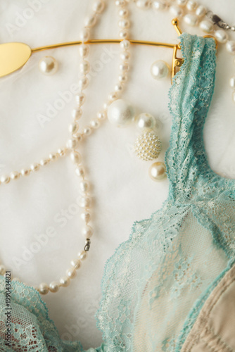 Details of the mint-colored delicate lace bra, gold hanger, and pearl embellishments. Film grain has been added to the photo.