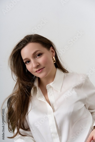 Woman with long hair sitting in a chair wearing a white button-up shirt in a bright room during daytime