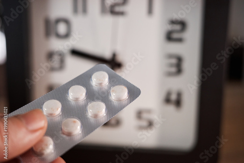 Holding a blister pack of pills near a clock while it is time for medication in a home setting