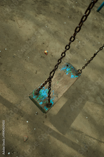 Swing set in a playground showing wear and tear with a dirt ground and minimal litter near the chains
