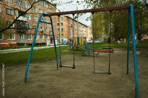 Swings stand still in an empty playground next to apartments on a cloudy day in the city