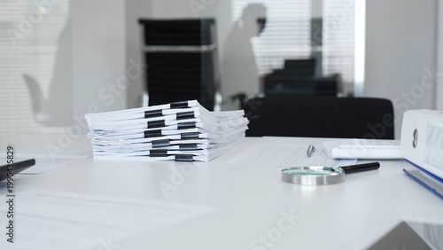 Bild auf Leinwand Office desk with stack of paper and magnifying glass, symbolizing heavy bureaucracy and business workload