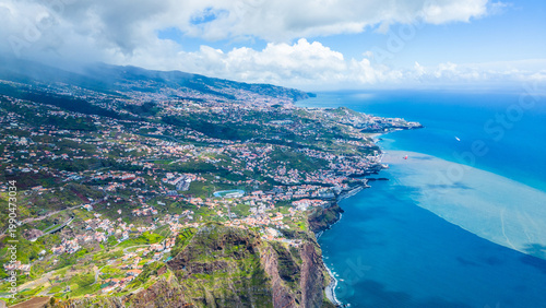 Funchal, Madeira's capital, sprawls across volcanic hillsides to the Atlantic. Lush landscapes meet the vibrant blue ocean under a partly cloudy sky. Cabo Girao