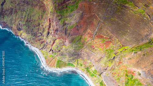 Aerial view of Madeira's dramatic coastline Cabo Girao, showcasing vibrant blue ocean, rugged cliffs, and verdant terraced fields clinging to the steep slopes.