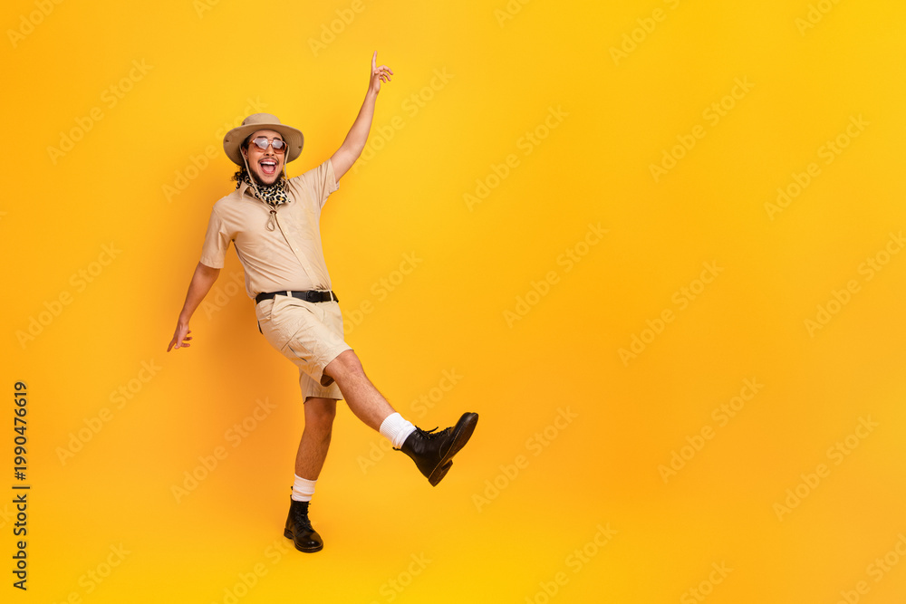 Obraz premium Dynamic traveler in safari outfit dances with joy against bright yellow backdrop
