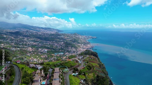Funchal, Madeira's capital, sprawls across volcanic hillsides to the Atlantic. Lush landscapes meet the vibrant blue ocean under a partly cloudy sky. Cabo Girao