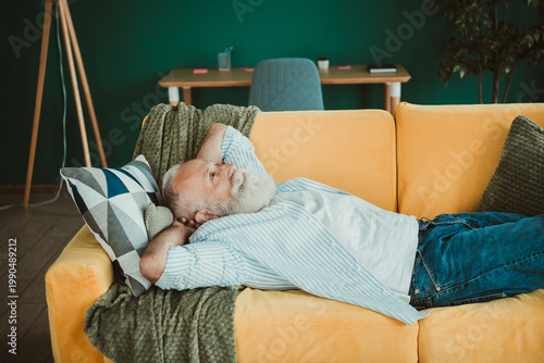 Tableau sur toile Calm senior man rests on bright orange couch at home in cozy living room scene i