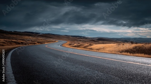 Serpentine Country Road Under Dramatic Clouds in Autumn Landscape with Golden Grass and Scenic Horizon