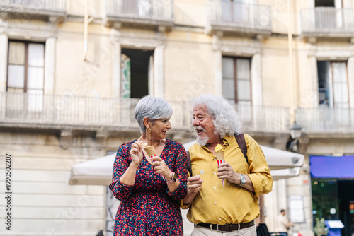 Happy senior adult friends sharing a moment, eating ice cream cones while strolling in a charming european street