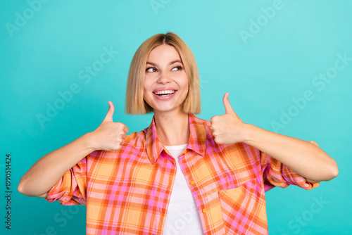 Quadro em tela Smiling young woman giving two thumbs up in casual plaid shirt against bright tu