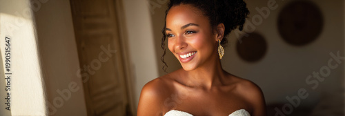 An Afro-American bride stands in a garden during sunset. She wears a simple bridal dress and a necklace. Her smile brings warmth to the moment as she enjoys her special day
