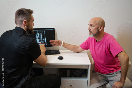 Two males discussing medical spine image in consultation room