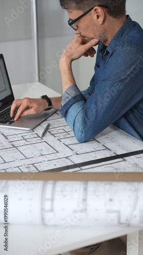 Tableau sur toile Architect man working on a laptop, analyzing blueprint plans and residential bui