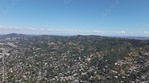 Aerial wide shot of Sherman Oaks neighborhood in Los Angeles during summer, showing dense residential homes across rolling hills under clear blue sky. Suburban sprawl and urban landscape in USA.
