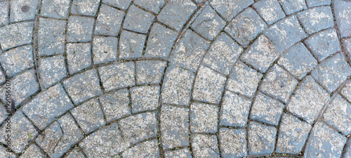 Top view of a floor made of rectangular gray stones, forming a beautiful geometric design with curves. Floor worn by time, with small specks of dirt in its crevices. Daylight.