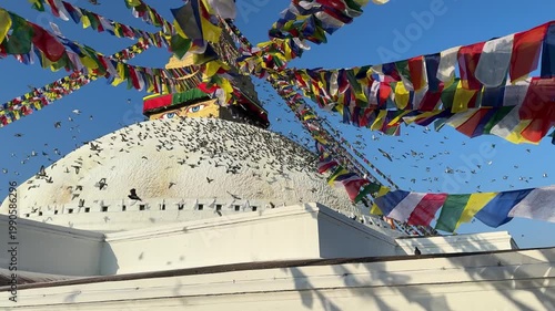 Slow motion pigeons flying around Boudhanath stupa in Kathmandu with colorful prayer flags waving in the wind. Spiritual atmosphere, Buddhism, travel, peaceful scene, cultural landmark