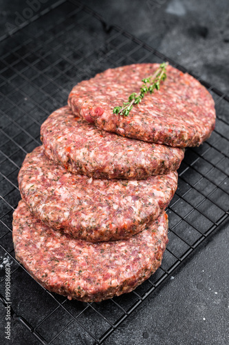 Raw mixed beef and lamb patties with herbs and pepper on dark stone background. Minced meat cutlets with copy space for cooking.