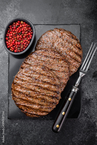 Grilled beef lamb meat burger cutlets  with juicy texture and browned crust. Overhead flat lay on dark stone background for menus.