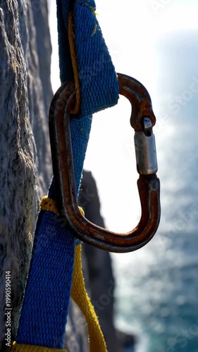 Close-up of climbing carabiner and harness on rock face, safety equipment, climbing gear.