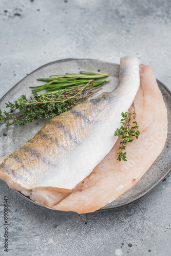 Raw pike perch fillets with skin and fresh herbs on light background, lean freshwater white fish for healthy cooking.