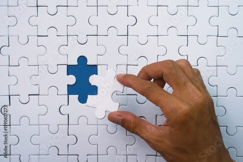 Human hand carefully places the last white puzzle piece into place