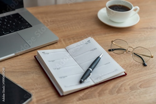 Open planner beside laptop and glasses, pen resting on weekly spread, steaming coffee cup in soft morning light, tidy wooden desk evokes calm productive routine and schedule focus