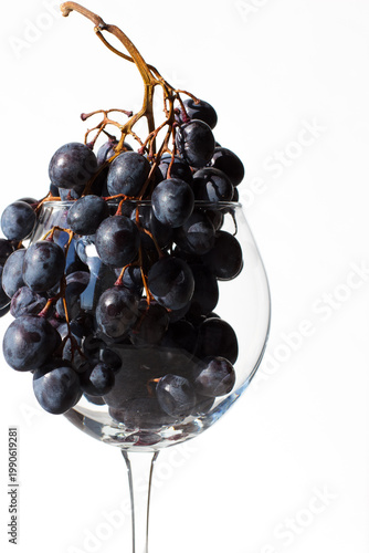 A glass with red grapes on a white background. Close-up. The glass on the left side