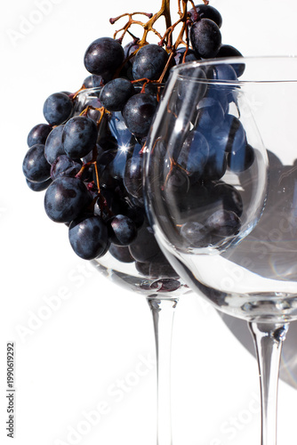 Two wine glasses on a white background. Empty glass and glass with red grapes. Close-up photo