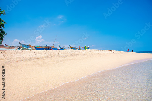 Fotografie Sandy Shore Under a Clear Blue Sky with Fishing Boats in Galle, Sri Lanka