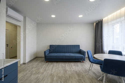 modern living room with a navy blue sofa, matching chairs, round dining table, light grey laminate floor, textured walls, recessed ceiling lights, sheer curtains, and an air conditioner