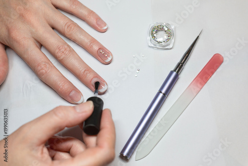 A woman is doing her manicure. She is gluing diamond rhinestones to her nails with nail polish.