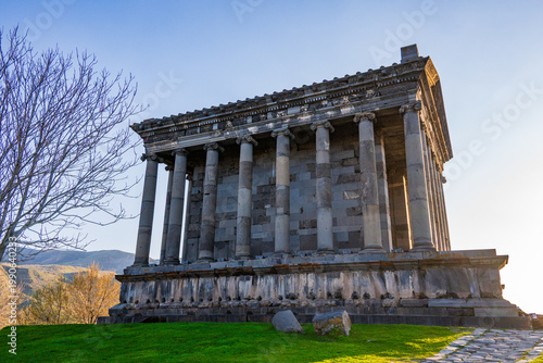 Konstfotografi Historic Garni temple ruins with tall columns, grassy field, mountains