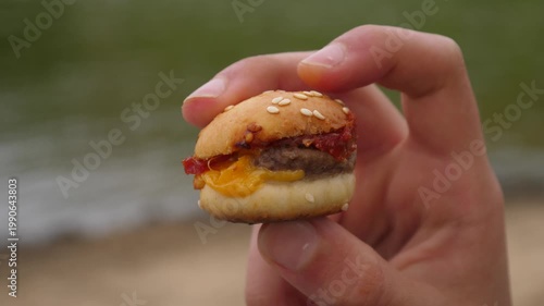 Closeup holding a small tasty burger with fingers showing its layers from side