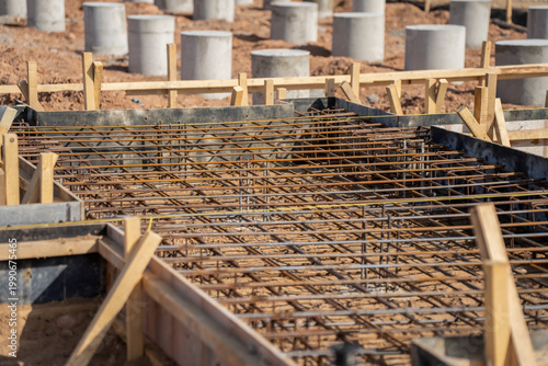 Rebar reinforcement mat inside concrete slab formwork on solar plant construction site with wooden bracing and concrete foundation sleeves visible