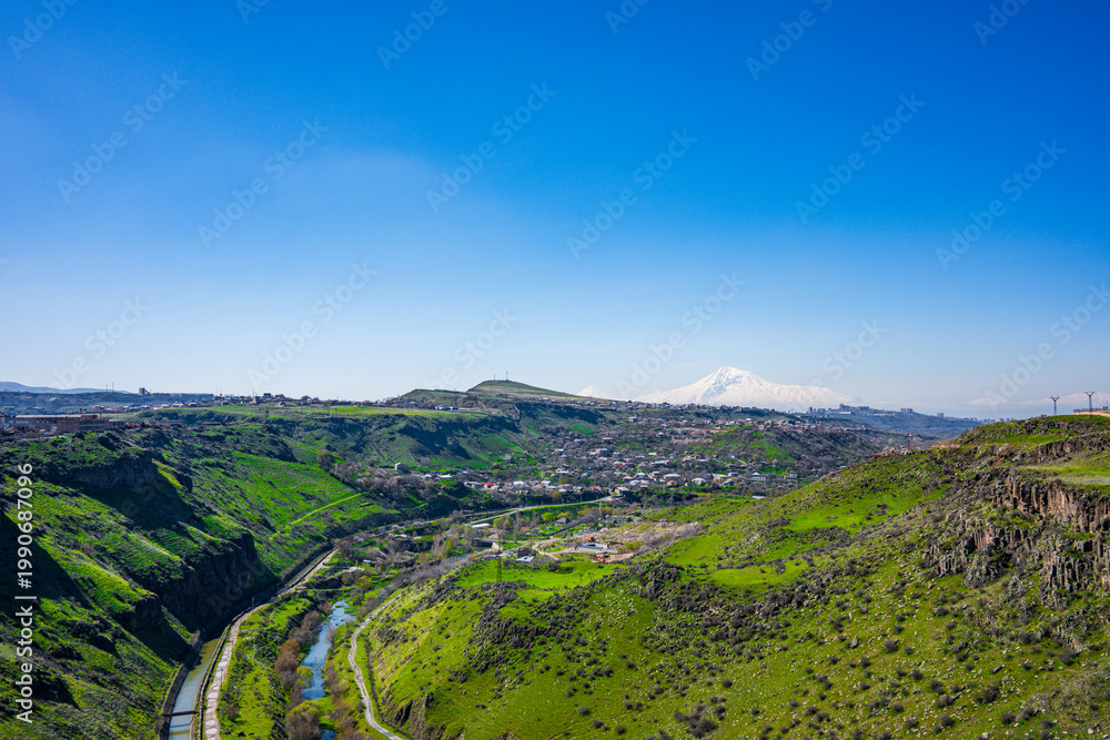 Fototapeta premium Scenic landscape of rolling green hills, river, and distant mountains