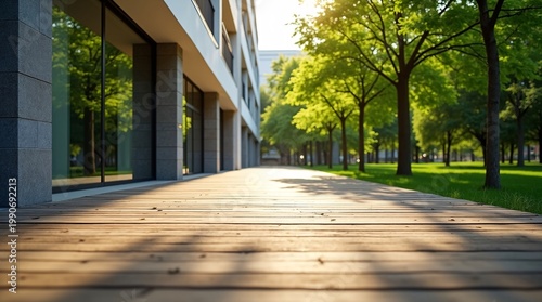 Sunlit wooden walkway flanked by modern stone building and lush tree-lined greenery