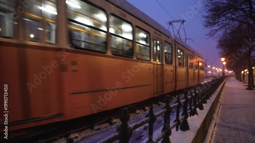Budapest, Hungary - January 6, 2026: Snow-covered tram tracks line the Danube embankment in Budapest at night, offering a wide view of the lit Buda Castle and Chain Bridge through falling snow.