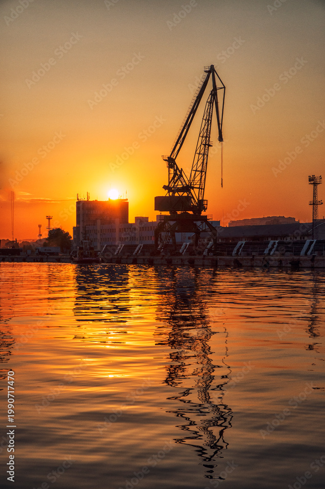 Obraz premium Fiery Sunset Over Port of Varna with Harbor Crane Reflected in Water. The photo is taken on 22.05.2016, Port Varna, Bulgaria.