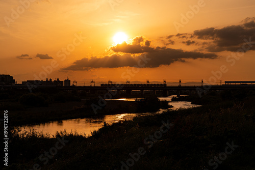 夕日の中で河川に敷かれた鉄橋と通行する電車