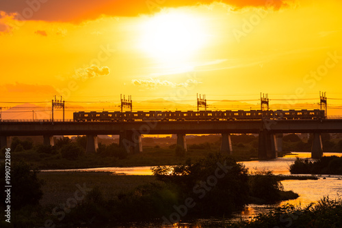 夕日の中で河川に敷かれた鉄橋と通行する電車