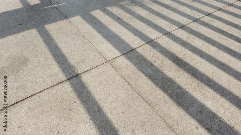 Fototapeta premium Geometric shadows on the concrete floor. Abstract composition of grid-like shadows on a concrete surface. Natural light creating striking geometric lines and patterns.