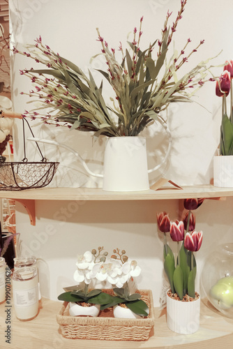 Artificial tulips and flowers in a white vase on display in a store window. Household goods, wicker basket, storage jars.