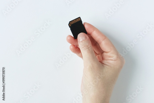 A black micro SD memory card in the hand of a Caucasian woman. White background.