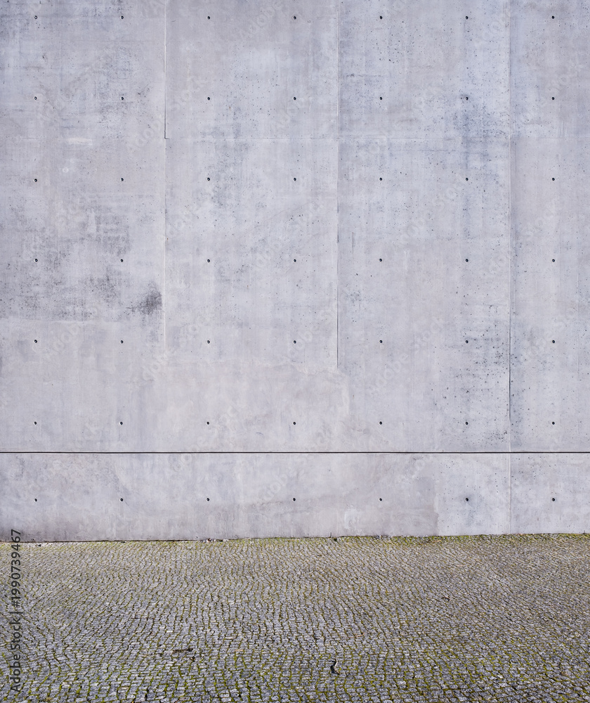 Fototapeta premium Tall raw concrete wall with formwork bolt holes above cobblestone pavement
