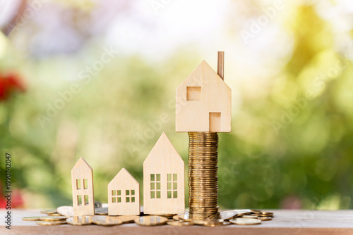 The image from the mirrorless camera shows a home model put on the stack gold coin with growing in the public park, Savings money for buy house and loan to business investment for real estate concept.