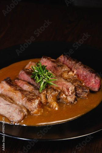 Detail of sliced roasted meat with rosemary and gravy on dark plate