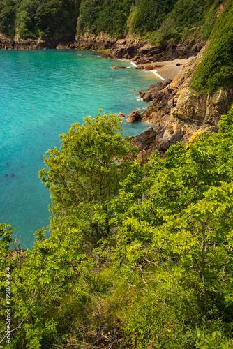 Scenic coastal landscape of Guernsey, Channel Islands, with turquoise sea, rugged cliffs and lush greenery.